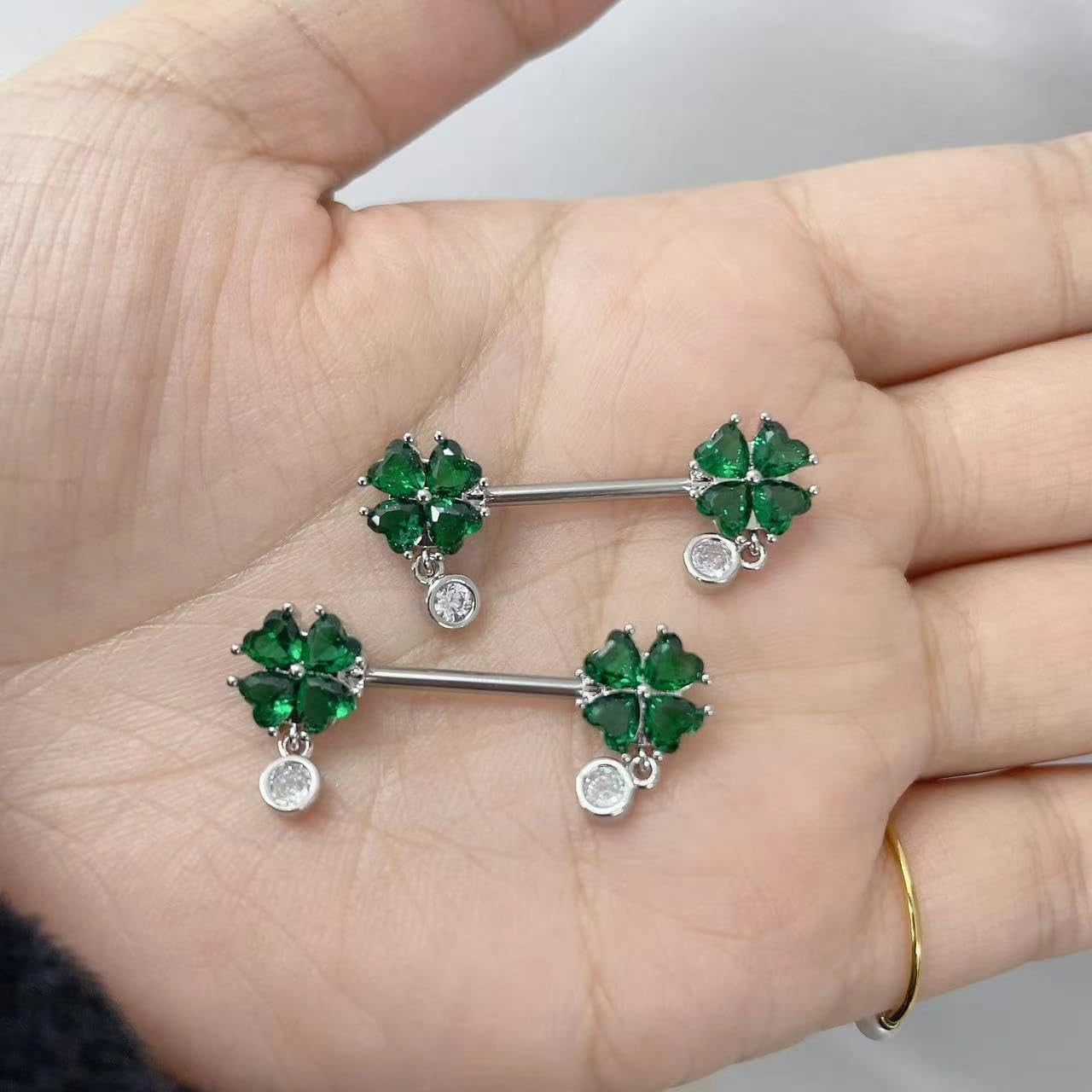 High-quality close-up of the cubic zirconia clover, highlighting its brilliant green color and secure prong setting on a nickel-free surgical steel bar.